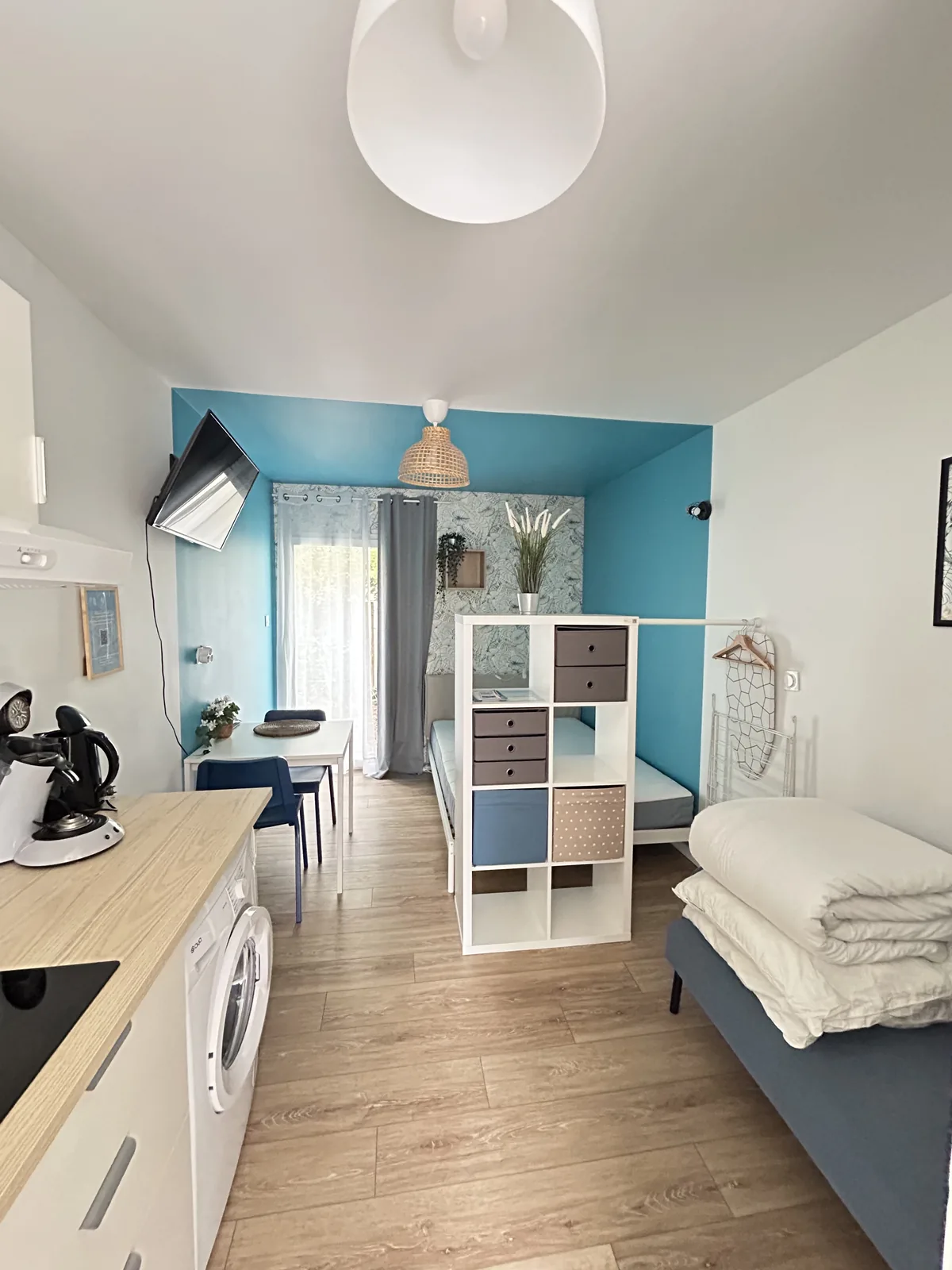 Vue d'ensemble du studio : kitchenette, coin repas et coin nuit séparé par une étagère
